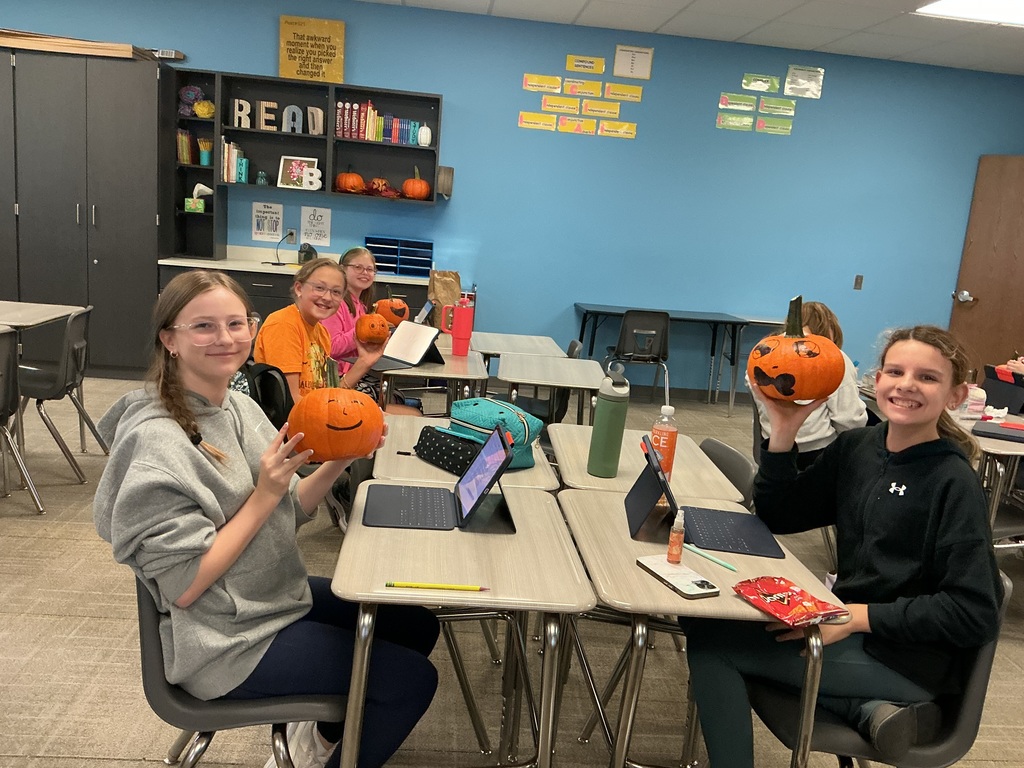 Photo of four students posing holding pumpkins with faces drawn on them.