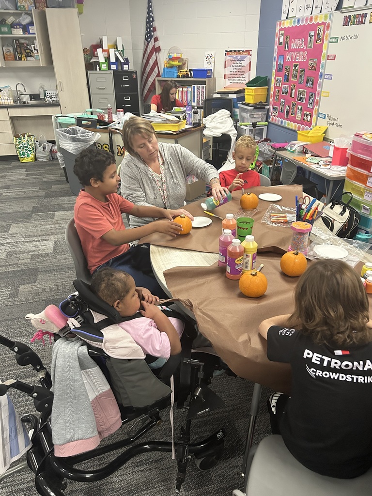 4 students sit with a table at a table painting small pumpkins.