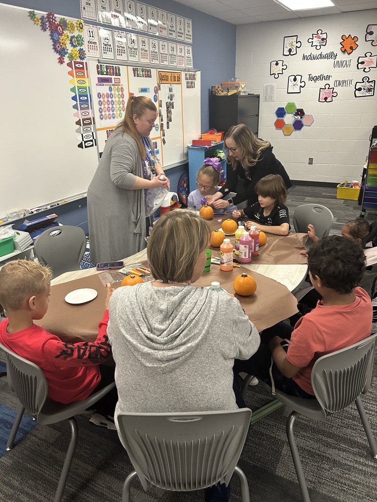5 students and 3 adults are seated around a table painting small pumpkins.