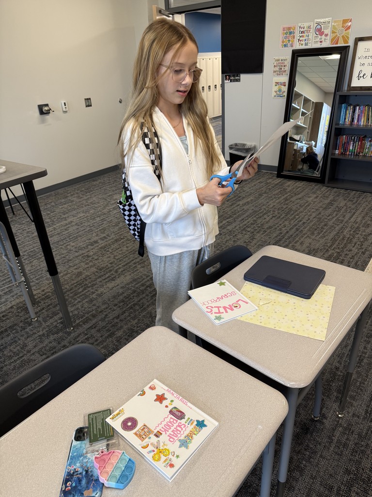 A girl in a white sweatshirt is standing up and cutting out pieces for her scrapbook page. 