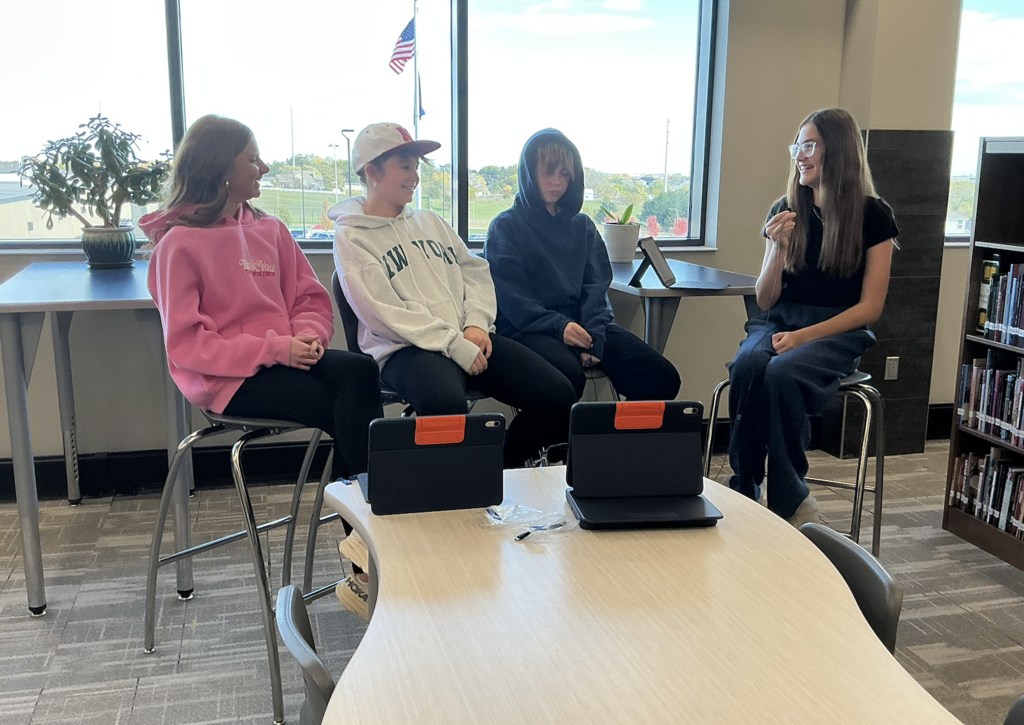 Photo of students sitting in chairs looking at each other while recording their talk show.