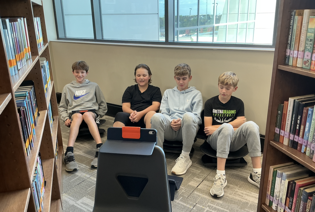Photo of students sitting on the floor with an iPad propped up recording their talk show.