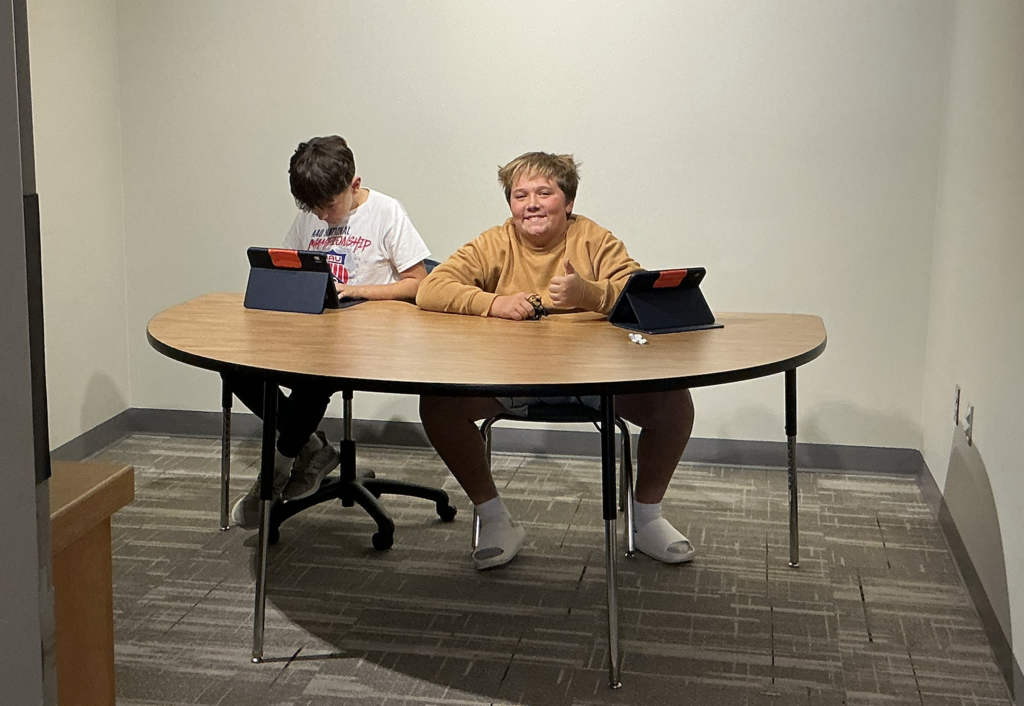 Photo of two students sitting at a table working on their iPads.
