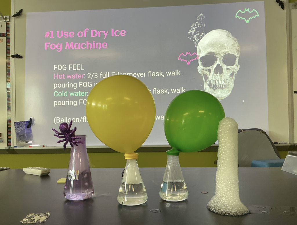 Photo of science experiment. There are four beakers: one with a spider, two with balloons, and one that is foaming.