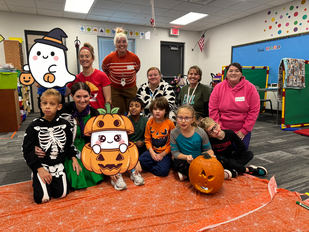 A group of students and paras sit on an orange cloth with their carved jack-o-lantern.