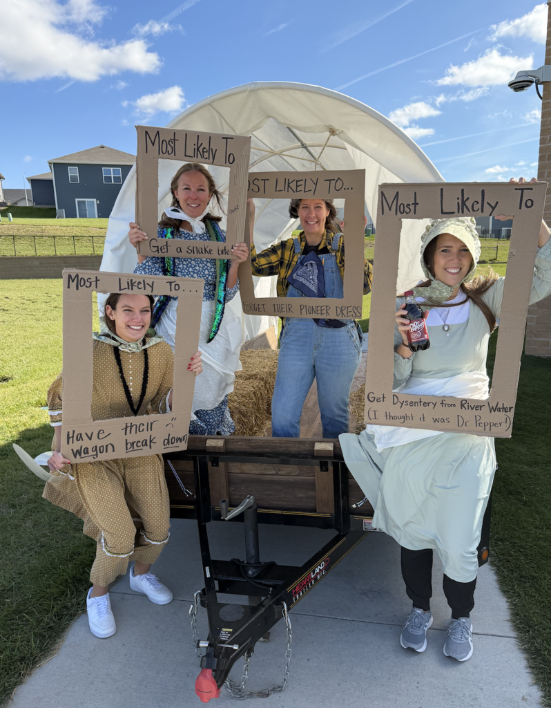 teachers posing in costume as the wild west by a covered wagon