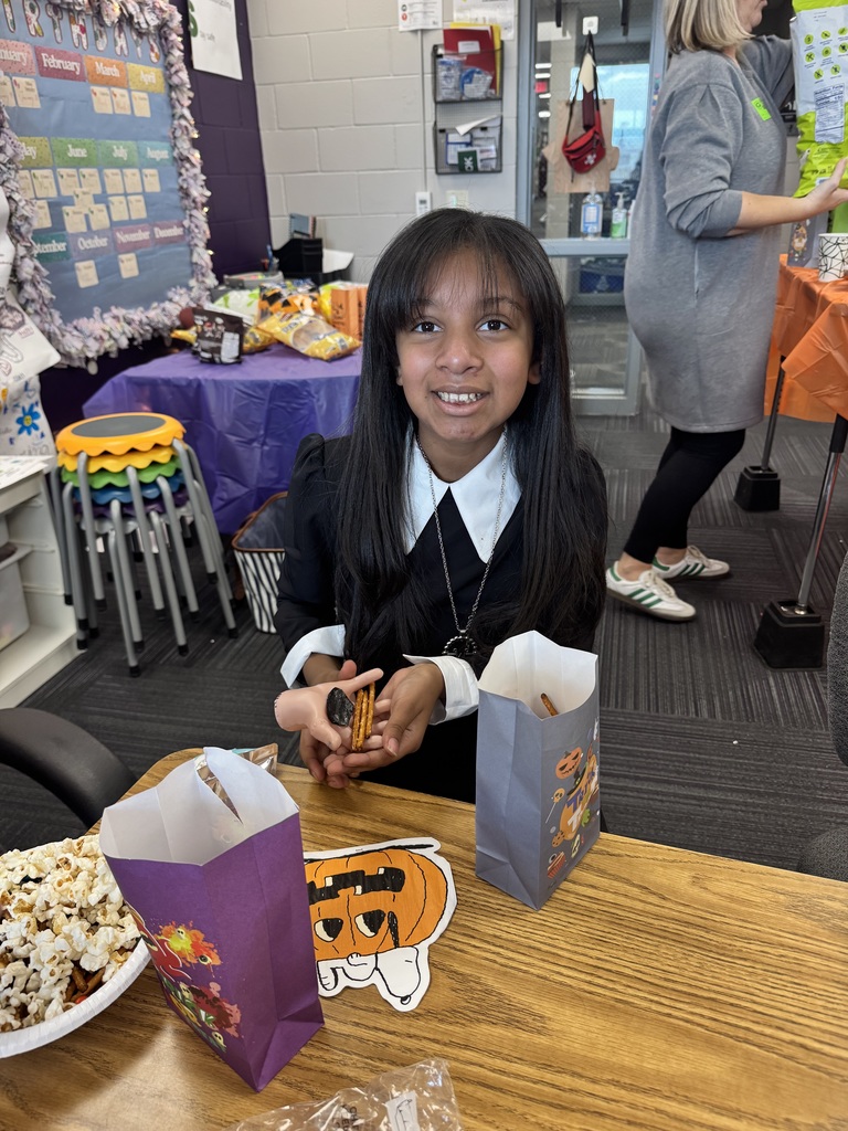 Girl dressed with a black and white shirt standing in front of a table while holding pretzels.  