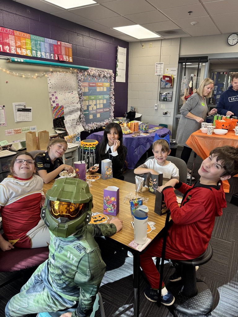 Group of children gathered around a table while eating out of a paper bag with Halloween decorations present.