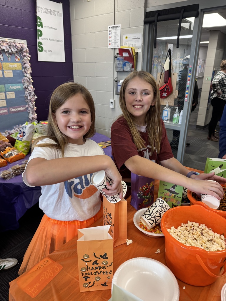 Two girls smiling while filling up a paper bag with popcorn.