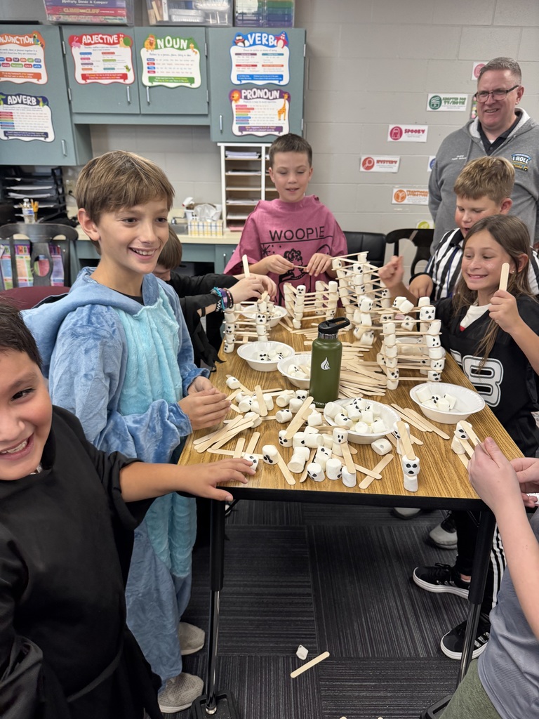 Group of children gathered around a table with a craft of popsicles sticks and marshmallows on the table.