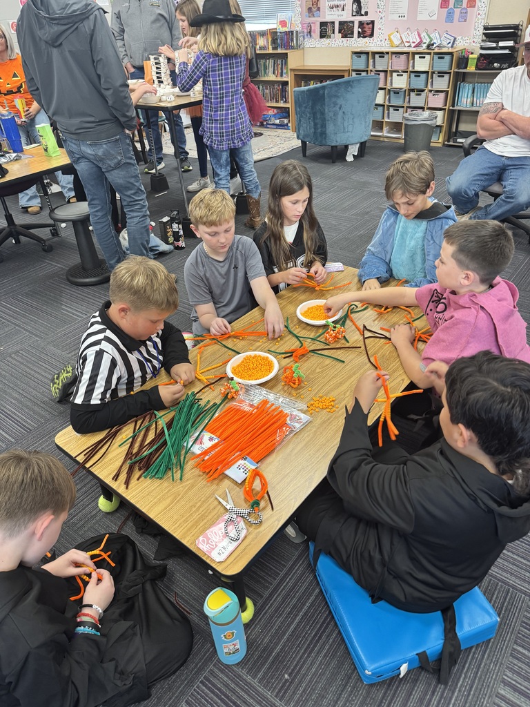 Group of children wearing costumes sitting at a table with orange and green and brown craft sticks present.