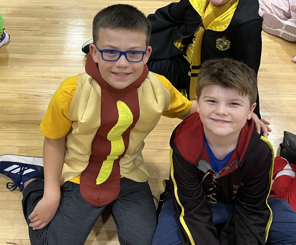 Two boys dressed in halloween costumes sitting on a gym floor.