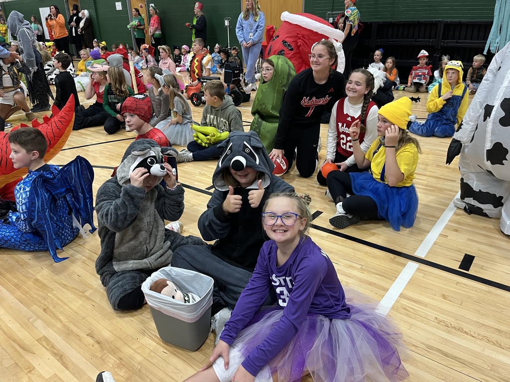 Three girls dressed in halloween costumes sitting on a gym floor.