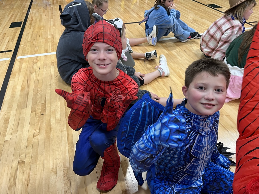 Two boys dressed in halloween costumes sitting on a gym floor.