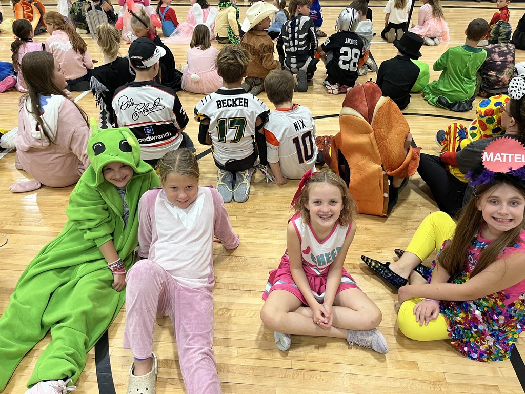 Four girls dressed in halloween costumes sitting on a gym floor.
