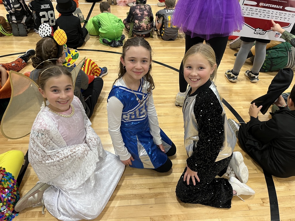 Three girls dressed in halloween costumes sitting on a gym floor.