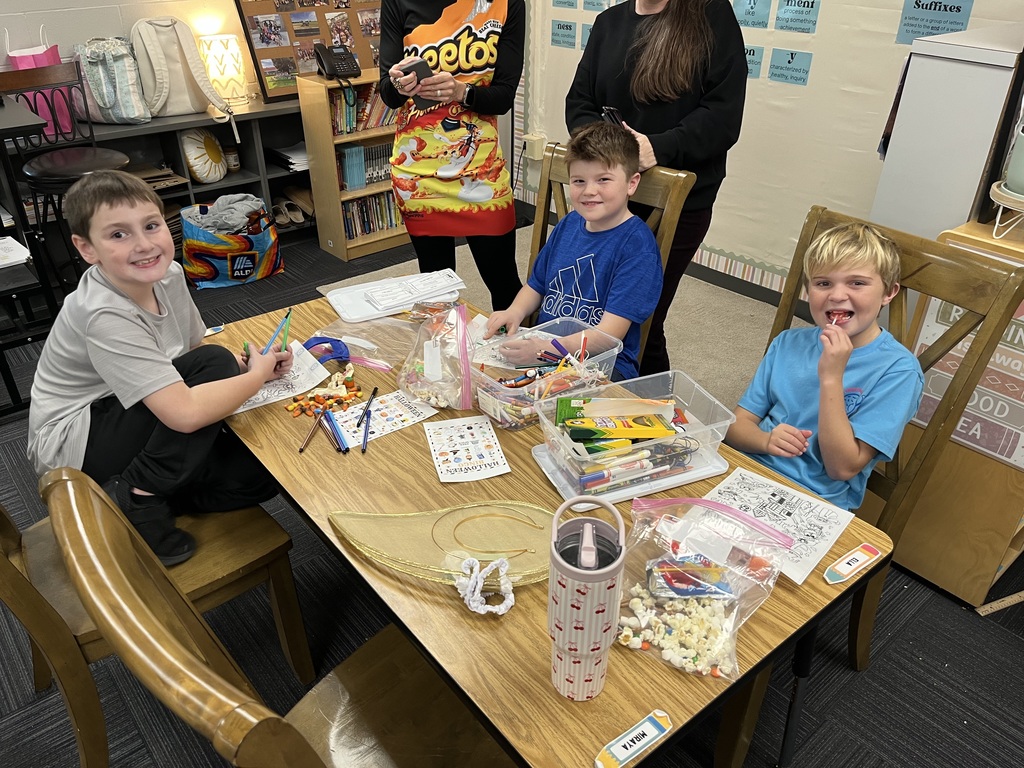 Three boys sitting around a table with art supplies like crayons and markers sitting on table.