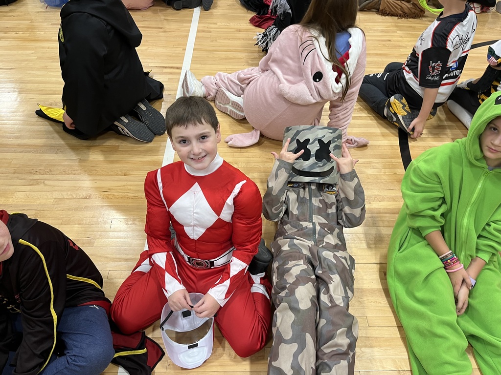 Four boys dressed in halloween costumes sitting on a gym floor.