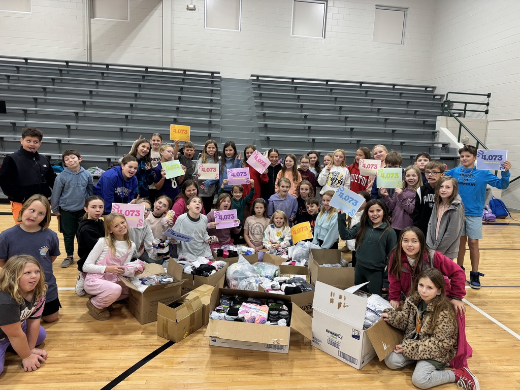 Group of children sitting on a gym floor holding up signs that show 4,073 with socks in boxes