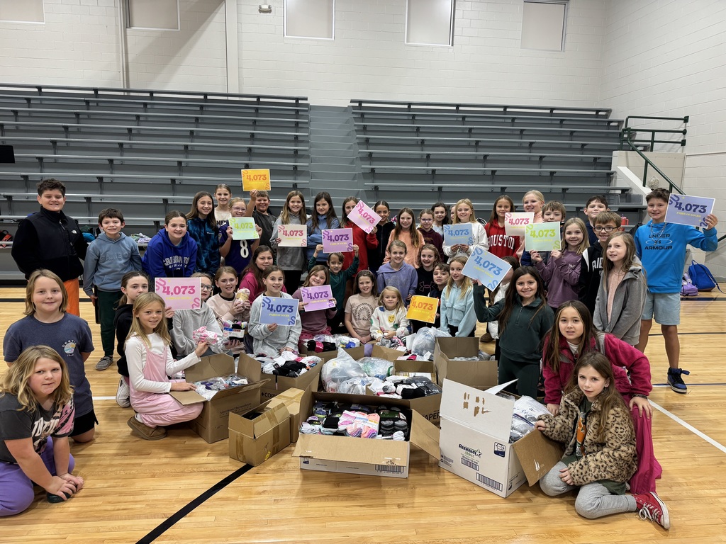 Group of children sitting on a gym floor holding up signs that show 4,073 with socks in boxes