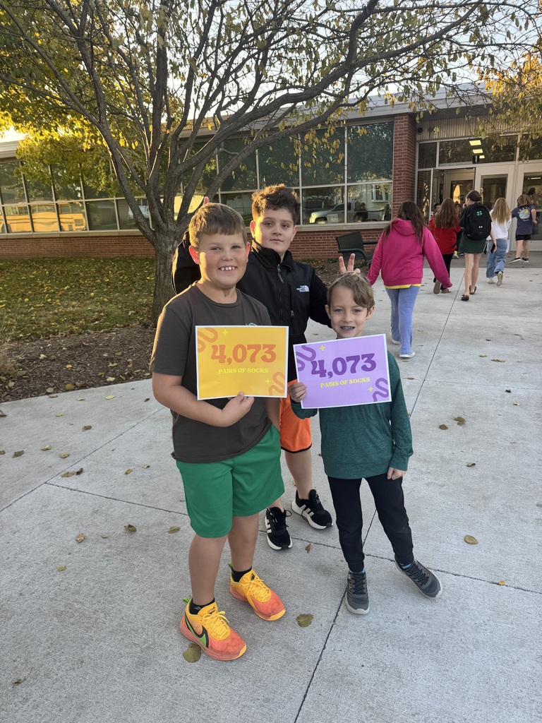 Three boys standing outside on a sidewalk, two boys holding a sign that shows the number 4,073
