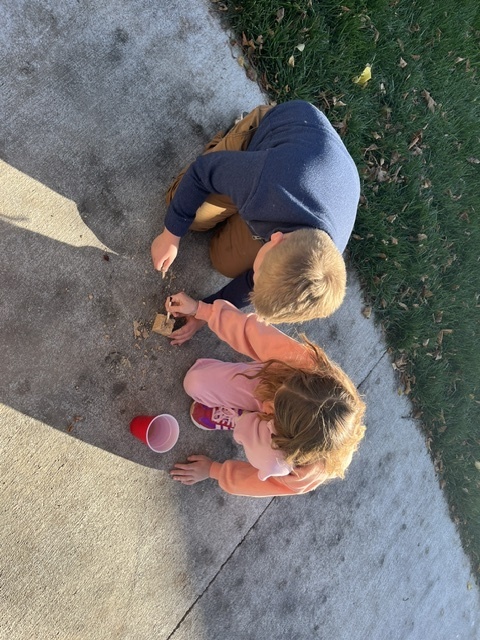Boy and girl sitting on a sidewalk digging through a block of rock and a red cup.