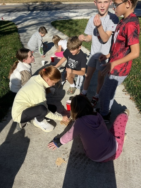 Group of students sitting outside on a sidewalk with sand and red cups visible.
