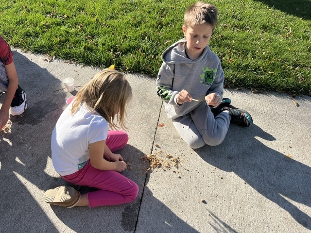 Boy and girl sitting outside on a sidewalk with sand on the sidewalk.