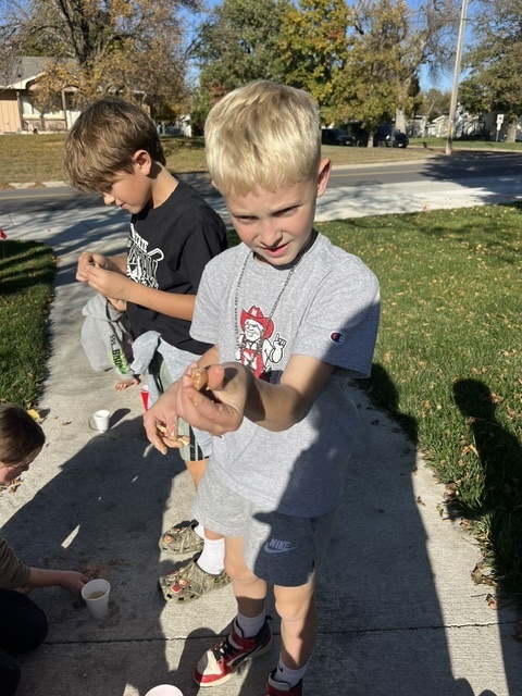 Two boys standing outside on a sidewalk holding a fossil in their hands.