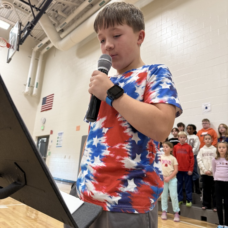 A fifth grade boy shares his essay in front of the school. 