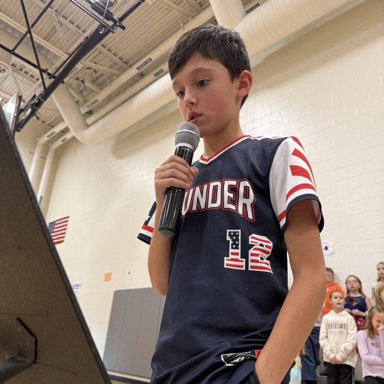 A fifth grade boy shares his essay in front of the school. 