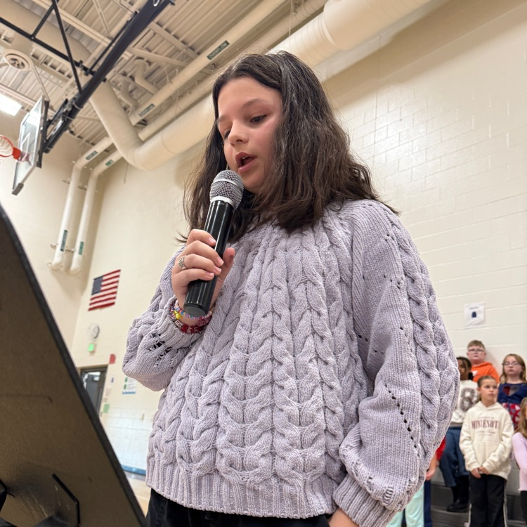 A fifth grade girl shares her essay in front of the school. 