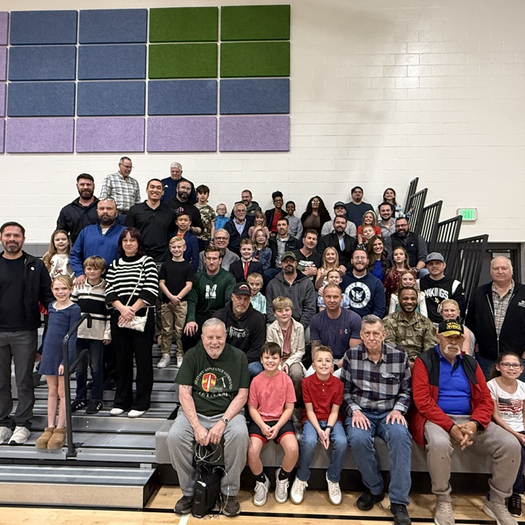 fourth graders and their veterans sit in the bleachers for a photo