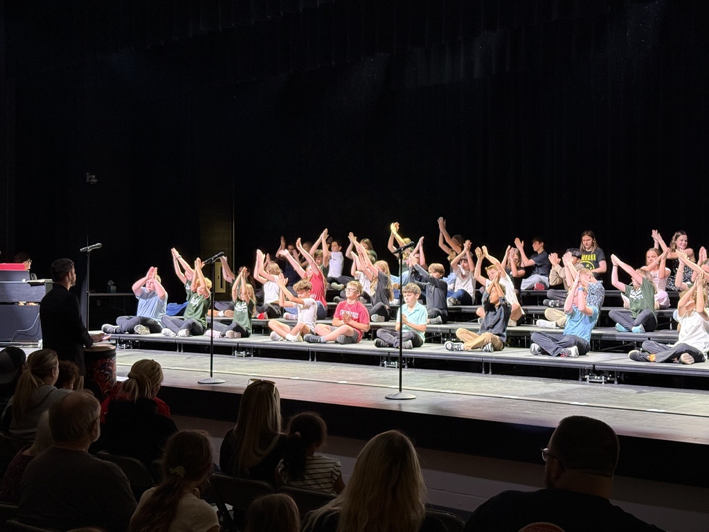 Photo of choir students seated on risers with hands in the air for their performance.