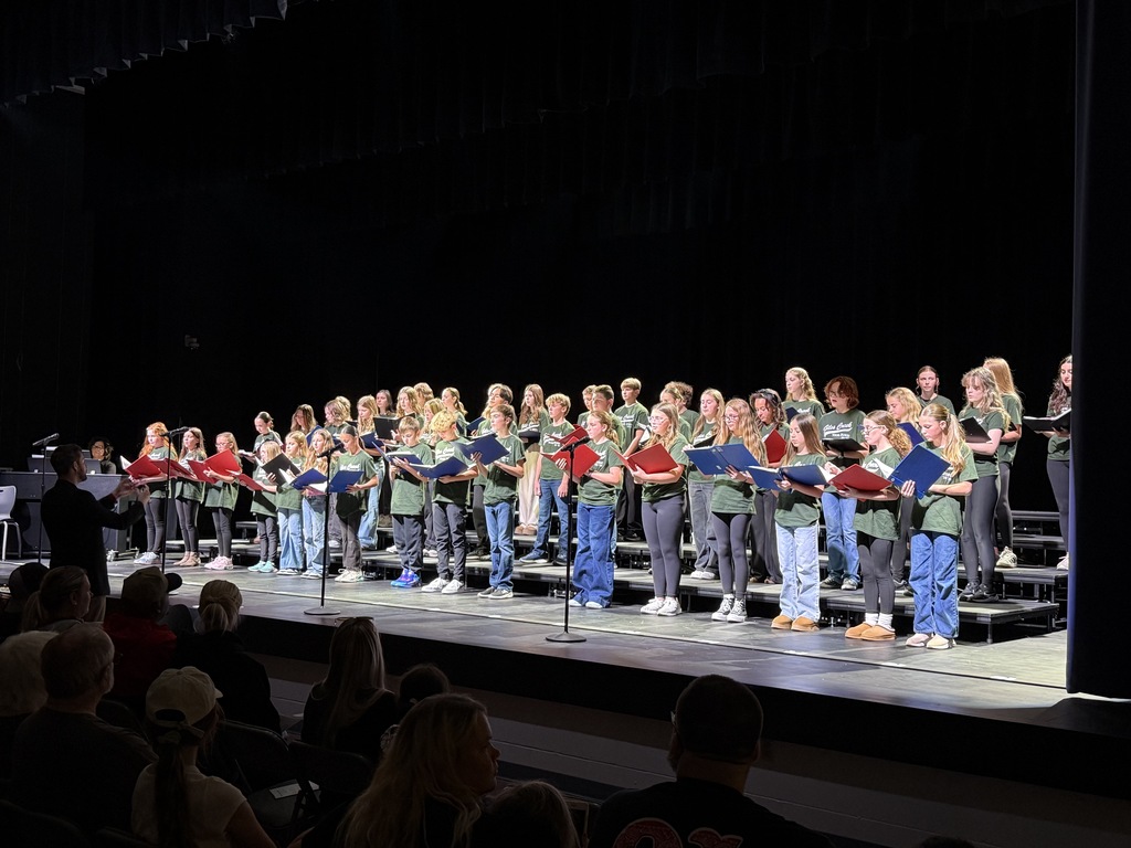 Photo of choir students standing on risers and singing with folders in their hands.