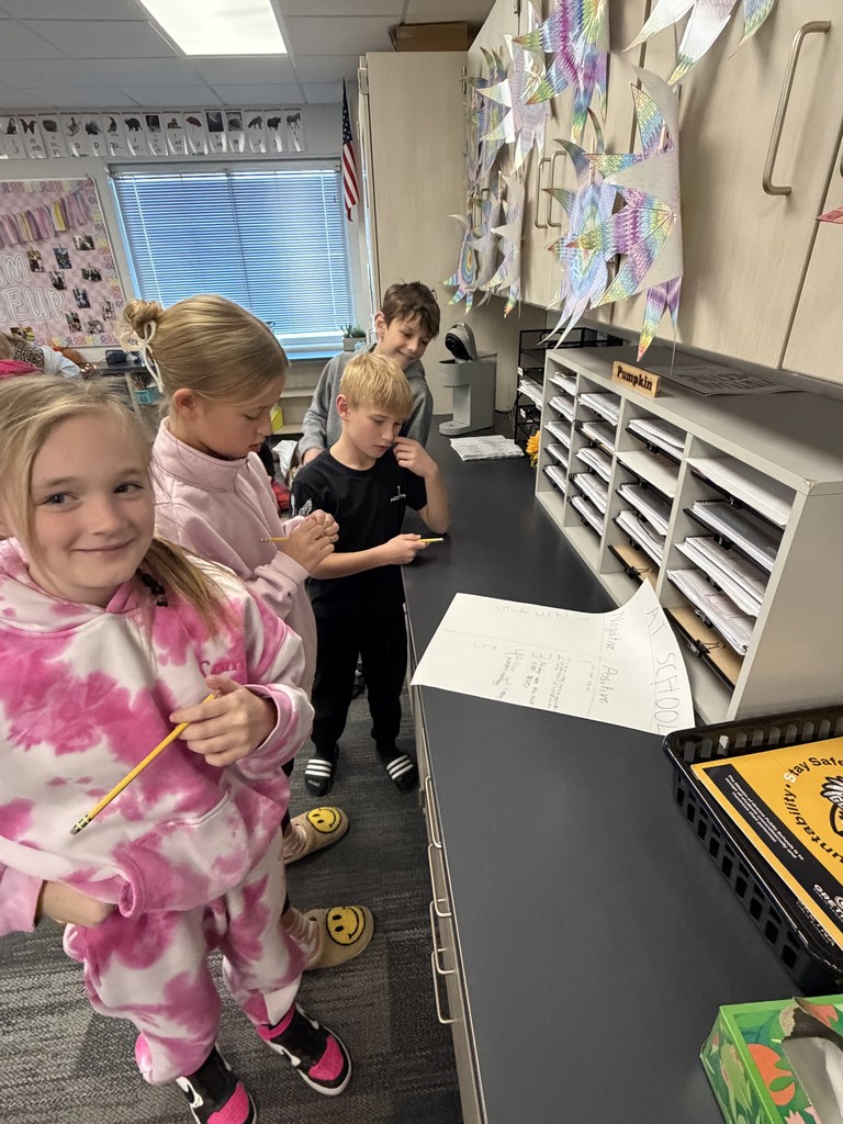 two fourth grade girls and two fourth grade boys are gathered around a counter working on a poster.