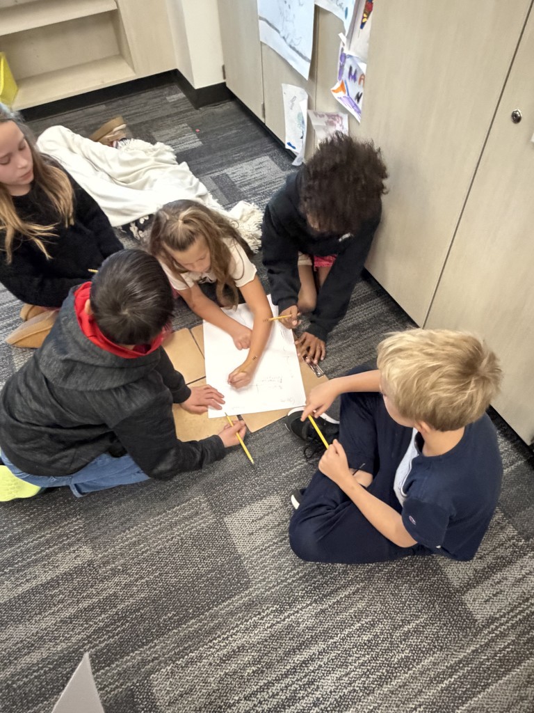 2 fourth grade girls and 3 fourth grade boys are gathered on the floor around a clipboard and paper.
