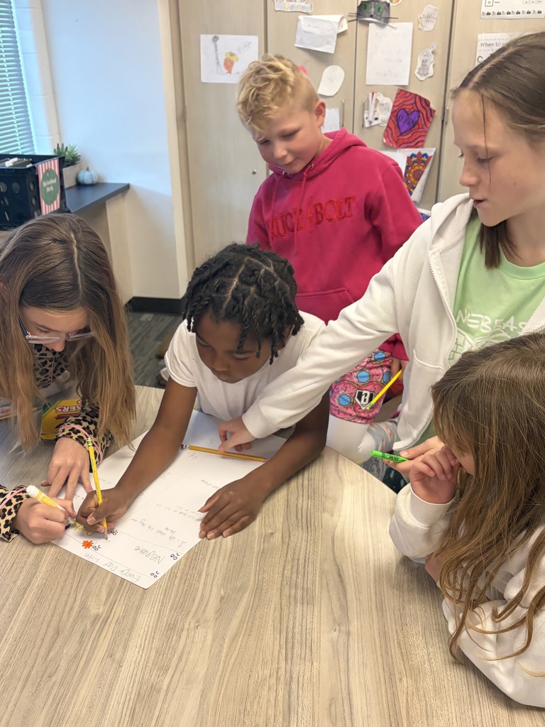 3 fourth grade girls and 2 fourth grade boys are around a table working on a paper.