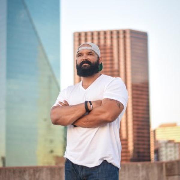 Stephen mackey speaks photo standing with arms crossed and city behind him