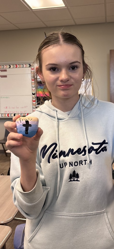 Photo of a student holding a rock with a cross and the word "trust" painted on it.