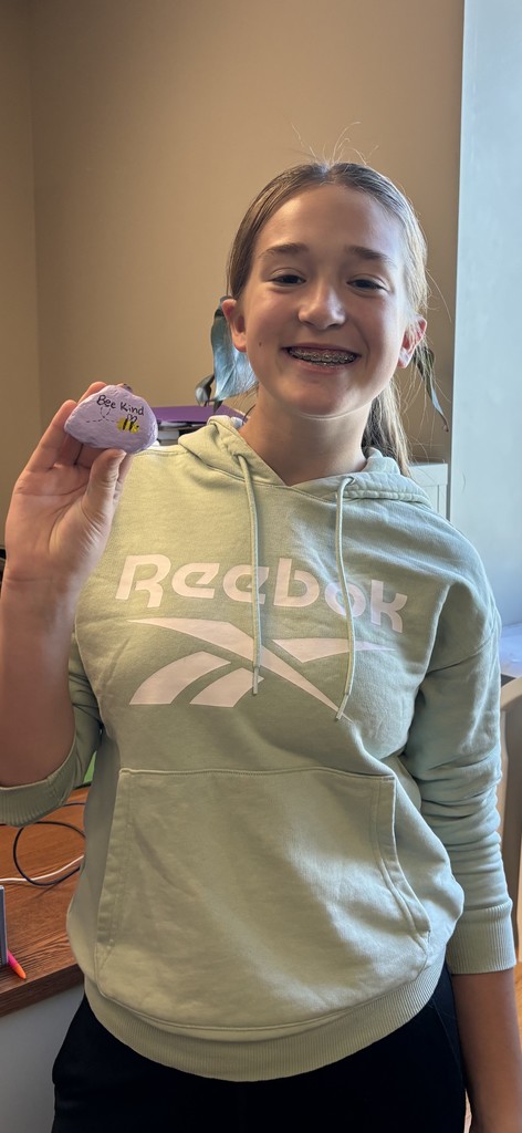 Photo of student holding a rock with a bee painted on it that says, "Bee Kind."