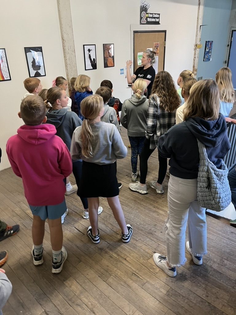 Group of students standing around an adult who is showing them a painting in an art studio.
