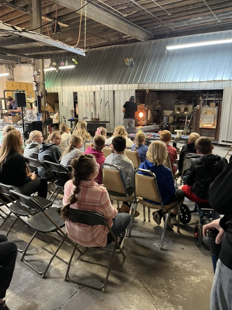 Group of students sitting in chairs gathered around a man who is putting pottery into a kiln.