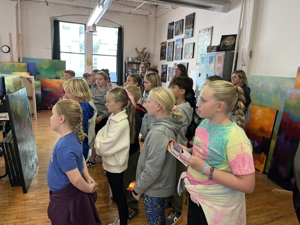 Group of students standing looking ahead in an art studio with paintings in the background.