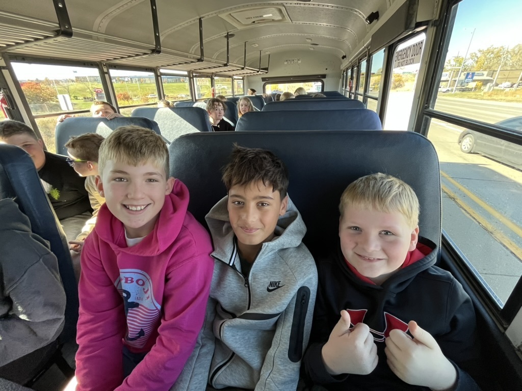 Three boys sitting on a bus smiling.