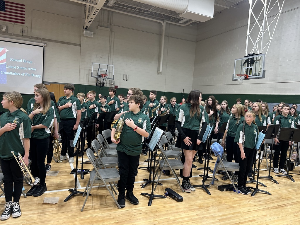 Members of a middle school band wearing green shirts holding their instruments and standing with hands on their hearts.