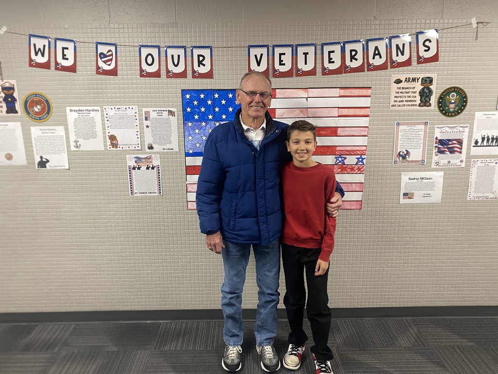 Student and his grandpa standing in front of a sign that says We Love Our Veterans