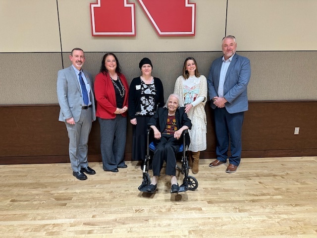 six individuals posing for the camera in front of the Nebraska "N" logo