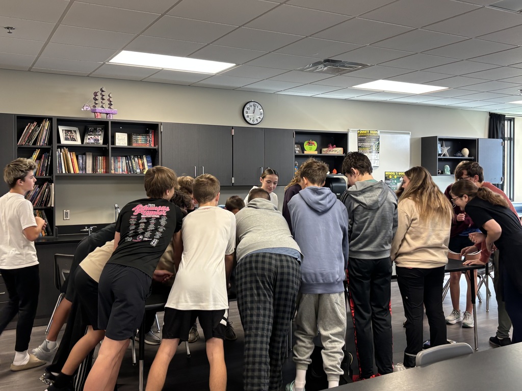 Photo of students around a table doing the tennis ball challenge.