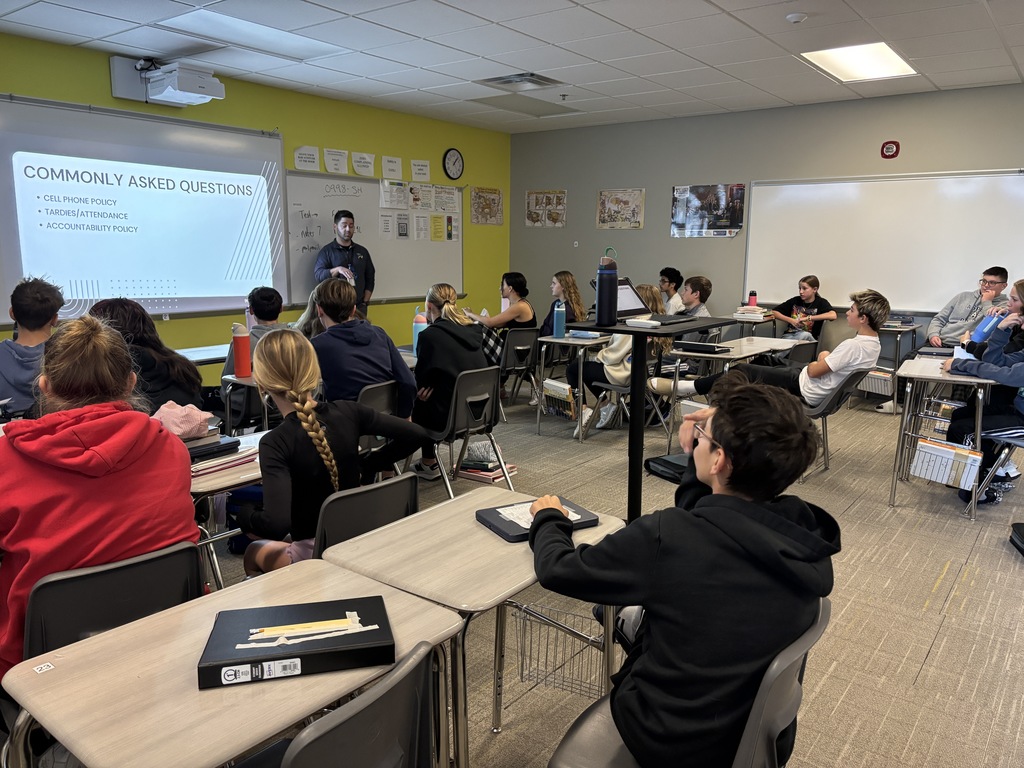 Photo of a high school counselor standing at the front of the room talking to students about the slide on the board that says, "Commonly asked questions."